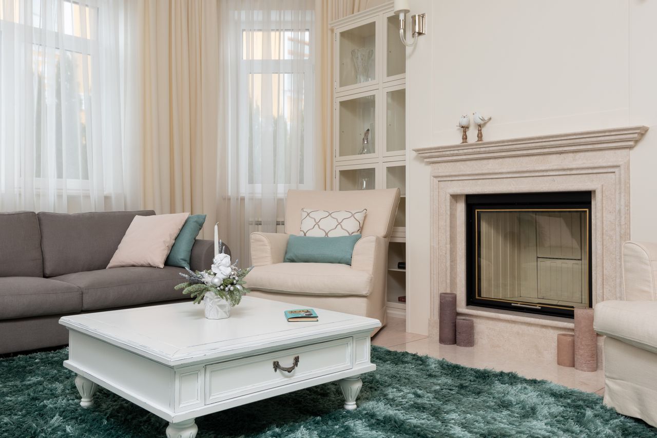 Interior of comfortable classic living room with couch and armchair on soft green carpet next to marble stone fireplace
